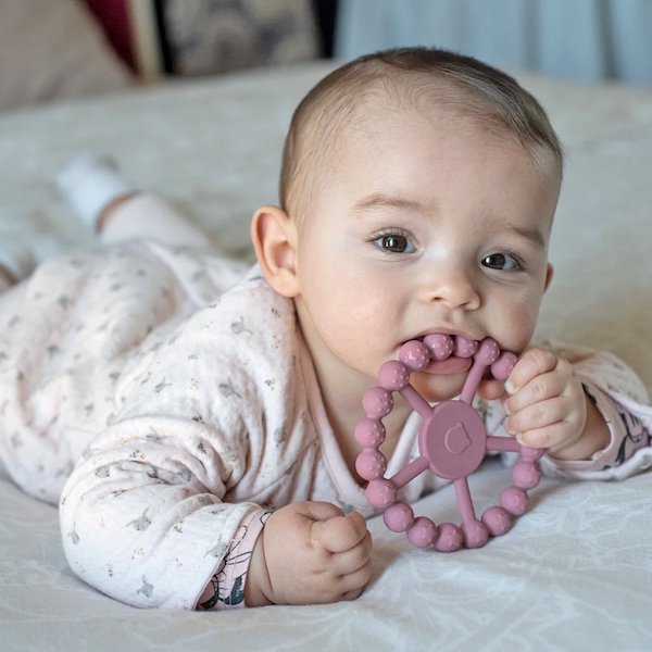 niña bebé con un mordedor de silicona de rueda de color morado